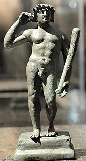 A grey-green statuette of a naked man holding a club in one hand.