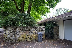 Photograph of a single-story house with white stucco walls and fronted by a rubblestone wall