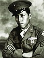 Head and shoulders of a young man wearing a peaked cap and a military jacket with ribbon bars and a badge on the left breast.