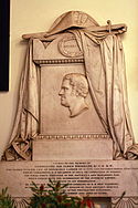 Photograph of a marble memorial carved with the image of James Brisbane in profile, carved cloth over the top and text on a panel beneath