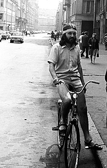 A long-haired man riding a bicycle on a city street
