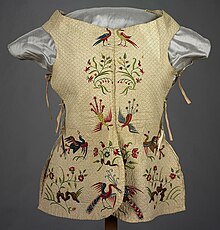 A garment resembling a quilted vest with ties at the sides. It is decorated with red and green embroidered birds and flowers.