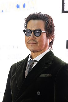 Toyokawa at press event in suit and tinted sunglasses looking toward left of camera