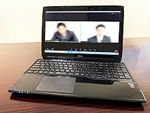 A laptop is sitting on a desk. The screen is divided in half showing blurred images of two people video conferencing.