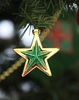 Weihnachtsbaumschmuck in Form eines goldenen Sterns, auf dem ein grüner Stern aufgebracht ist, der an einem Tannenzweig hängt