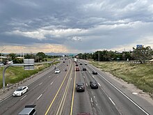 A six-lane freeway in a developed area with mountains in the distance.