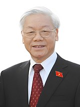 Nguyễn Phú Trọng standing in front of a white background, wearing a black suit, red tie and a National Assembly of Vietnam pin on his right chest.