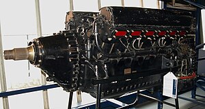 A front left view of a large black-painted aircraft piston engine. The engine is backlit by a window.