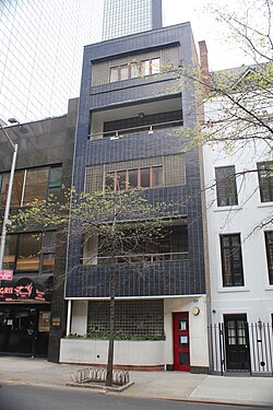The main facade of the building as seen from across the street. There is a storefront at the ground level and blue tiles on the other levels.
