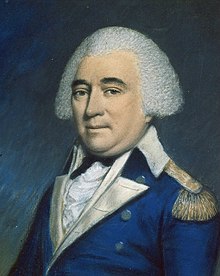 A man with white hair, wearing a blue jacket with gold lapels, buttons, and epaulets, a white shirt, and a black tie