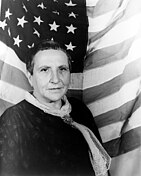 A black and white photo of a bald women in front of an American flag.