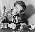 Woody Guthrie, wahrscheinlich in den 1940ern. Auf der Gitarre steht: „This Machine Kills Fascists“ („Diese Maschine tötet Faschisten“).