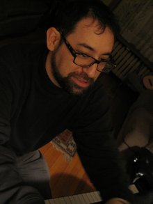 Perlstein seated at a baby grand piano, selecting music to play from a book of jazz standards, Chicago, 2013.