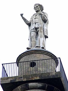 a stone statue of a man in Tudor clothes and down and cap and cahins off office holding a rolled up copy of maga carter