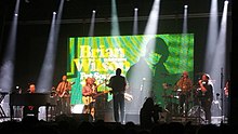 Wilson's large band onstage in front of an LED screen showing photos from the Pet Sounds era