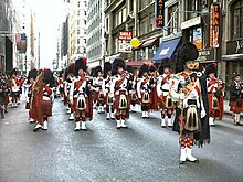 Red-kilted bagpipers in feather bonnets on an urban city street
