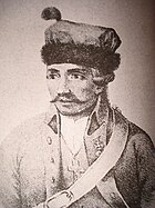 Black and white print shows a mustachioed man wearing a light colored military uniform and a fur hat.