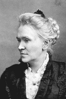 Portrait photograph of a middle-aged woman with her white hair in an up-do, and wearing a high-collared blouse.