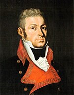 Painting shows a square-faced man with curly, light colored hair. He wears a dark blue military uniform with red lapels and a red sash over his right shoulder.