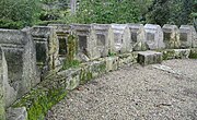 A row of mossy and weathered stones cut similarly as column segments, laid out in a curve to form a scalloped border in a garden.