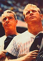"Two men in New York Yankee pinstrips stand attention with Yankee caps over their heart."
