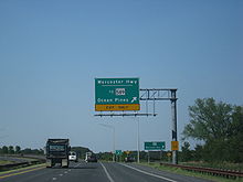 A divided highway curves to the left as the rightmost lane exits underneath an overhead green sign indicating the ramp leads to Worcester Highway and MD 589 toward Ocean Pines.