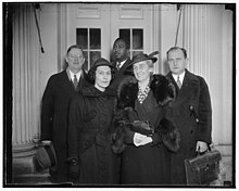 Five adults standing for a group photo: front is two white women; back row is two white men and a black man (center). They are indoors.