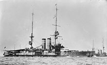 A large gray warship steams through the water; a second ship of the same type is in the background on a parallel course