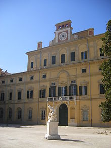 Façade of a yellow Renaissance palace under a blue sky, with a white marble statue in front of it.