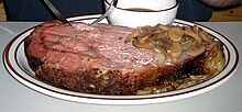 A slice of prime rib from a standing rib roast, topped (on the right side) with mushrooms