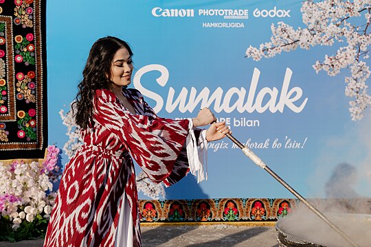 A woman in traditional clothes stirring sumalak during Navruz celebrations