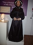 Madame Tussaud herself at Madame Tussauds in London. Her death mask is visible in the background on the left.