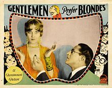 A lobby card for the 1928 film "Gentlemen Prefer Blondes." Actress Ruth Taylor is being proposed to by a gentleman on his knees.