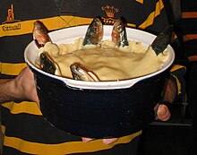 A blue ceramic dish containing a stargazy pie, with six fish poking out of a shortcrust pastry lid, looking skywards