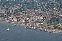An aerial picture of Downtown Edmonds, showing a city laid out in a grid of streets and buildings. The water takes up the bottom half of the picture, with a ferry approaching the dock.