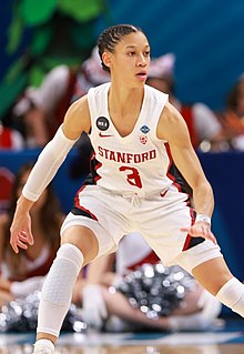 Anna Wilson in a white Stanford uniform, with white compression shorts visible under regular shorts. She is wearing a white compression sleeve on one of her arms and white compression sleeves on her legs.