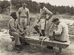 Two (standing) Bermuda Militia Infantry soldiers wearing the 1905 style khaki peaked cap, and two (seated) wearing the new khaki side cap, circa 1940