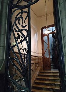 Entrance of Casa de los lirios, by Eduardo Rodríguez Ortega in Buenos Aires (1905). It features a black door made of metallic irises flowers, behind is the marble staircase and a wooden door, both in curvy organic shapes, behind that is the lift.