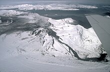 A circular, ice-filled plain with a steaming pit. Ice is covered with grey ash and one dark lava (?) flow