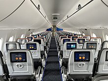 The inside of a plane is shown, with two seats per row on the left and three seats per row on the right. Each seat also has a personal television screen in front of it. The overall color scheme is gray.
