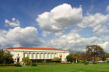 Huntington Library building with a green lawn in the foreground and white clouds in the sky.