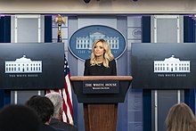 A 32-year-old woman conducting a press conference in the White House, specifically in the James S. Brady Press Briefing Room in West Wing of the White House.