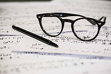 A pair of eye glasses and an ink pen rest on top of some sheet music