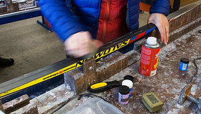 Smoothing of grip wax on a classic cross-country ski, using a hand-held "cork", like the item marked "Swix" in the right foreground.