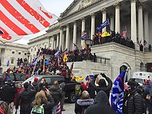Crowds of supporters are dense on the steps of the U.S. Capitol building, waving Trump flags.