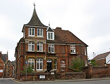 A red bricked building with a spired roof, windows and a black gate