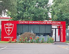 The front entrance gate of AC Monza's Centro Sportivo Luigi Berlusconi – Monzello, with trees in the background