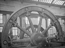 Flywheel; the hub and spokes cast in two halves, bolted at the hub with the rim assembled from ten castings. These are bolted to the spokes, held together by shrinking rings in the grooves.[72]
