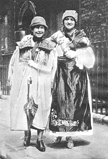 A woman with an umbrella and a woman in Croatian costume standing on a street