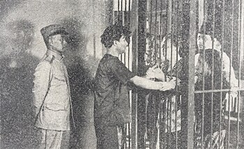 A shot from the film featuring Soebagio talking to people from behind bars, supervised by an officer